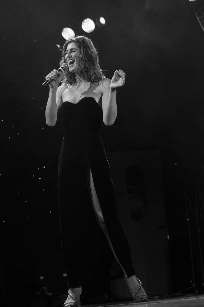 A woman named Daphne Always singing on stage at JoCo Cruise 2025, wearing a strapless black outfit and high heels.