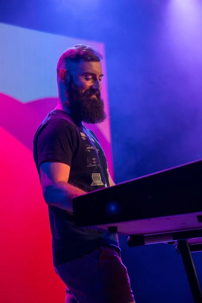 A man with a beard playing a keyboard on a colorful stage at JoCo Cruise 2025.