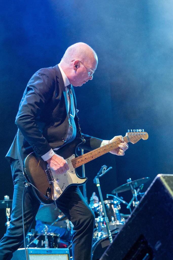 A musician in a suit playing an electric guitar on stage during JoCo Cruise 2025.