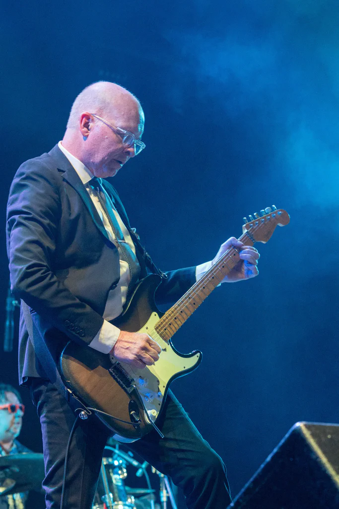 A man dressed in a suit playing an electric guitar on stage during JoCo Cruise 2025.