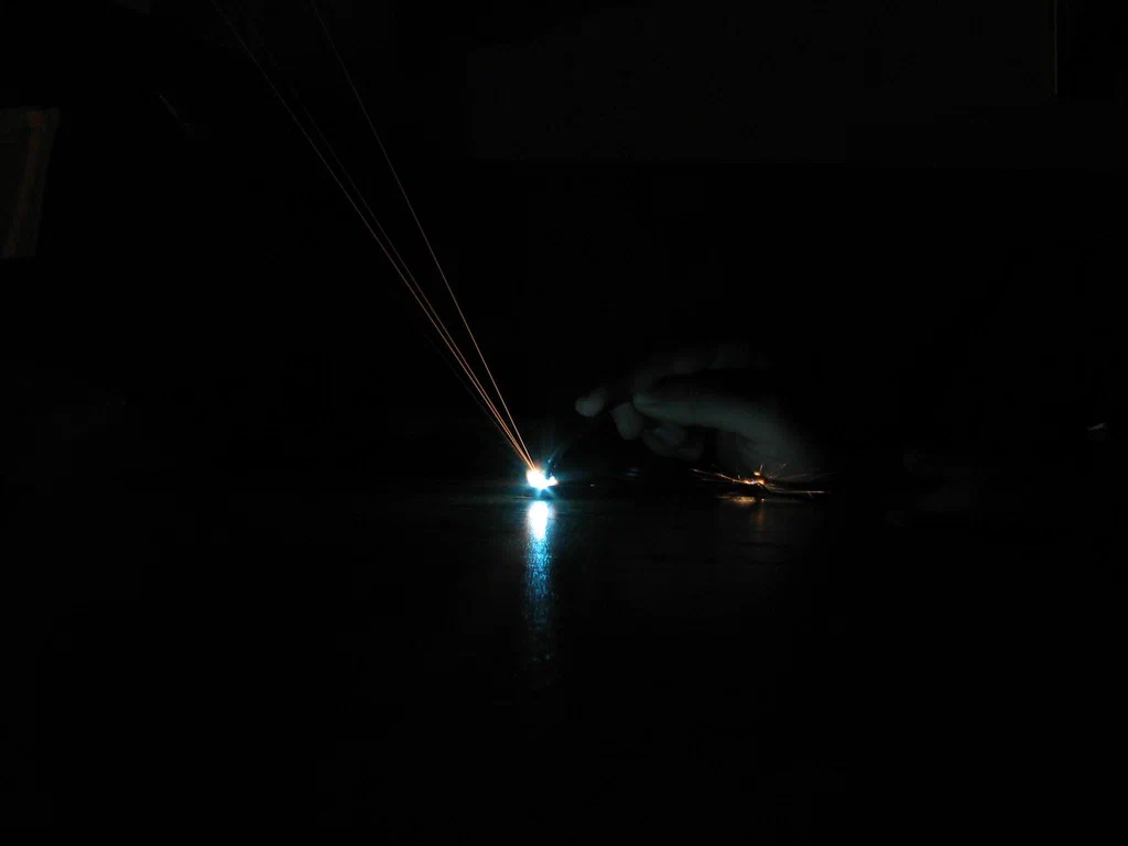 A high-voltage device sparks intensely, emitting bright blue and orange streaks of electrical discharge in a dark environment.