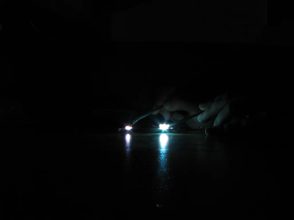 Close-up of a high-voltage device sparking, with bright electrical sparks and reflections on the surface below, set against a dark background.
