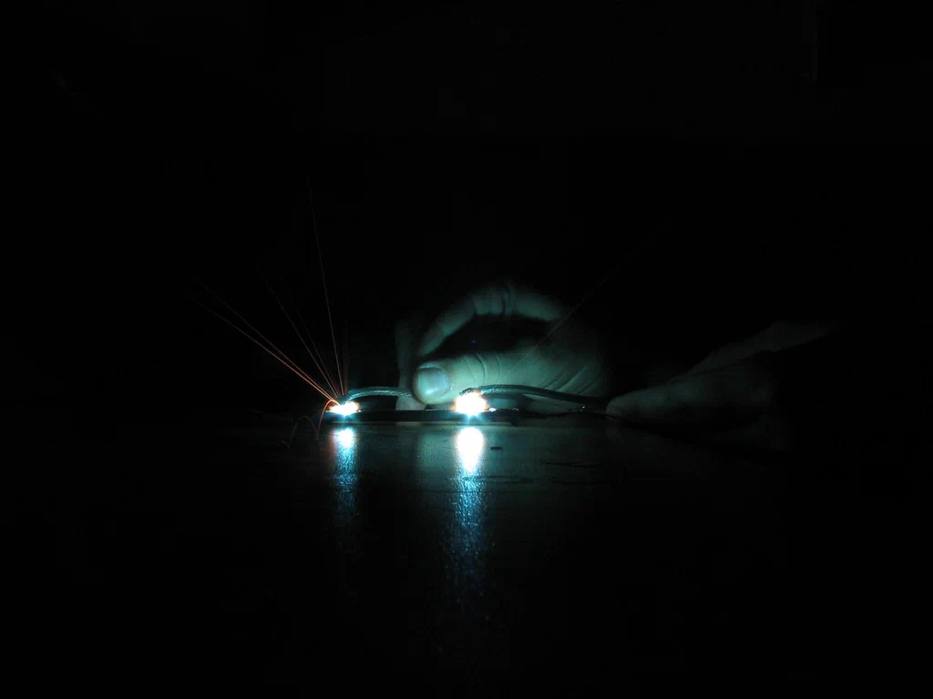 A person handling a high-voltage device, with visible sparks and electrical discharge in a dark environment.