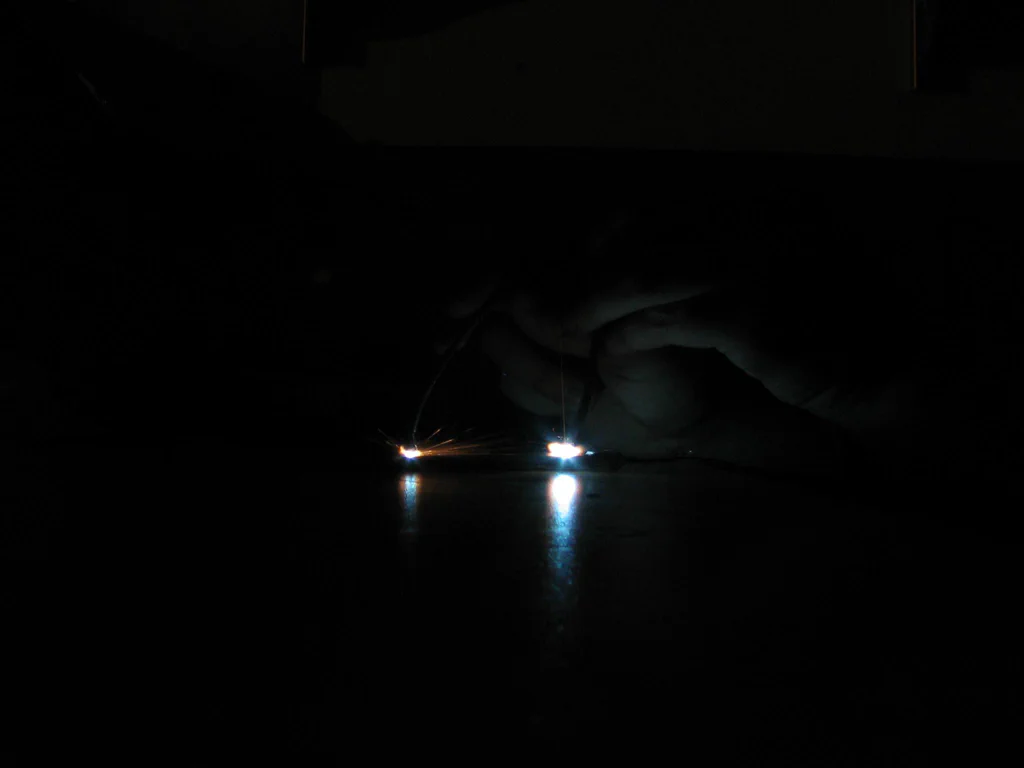 A person appears to be working with a high-voltage device, generating sparks in a dark environment.
