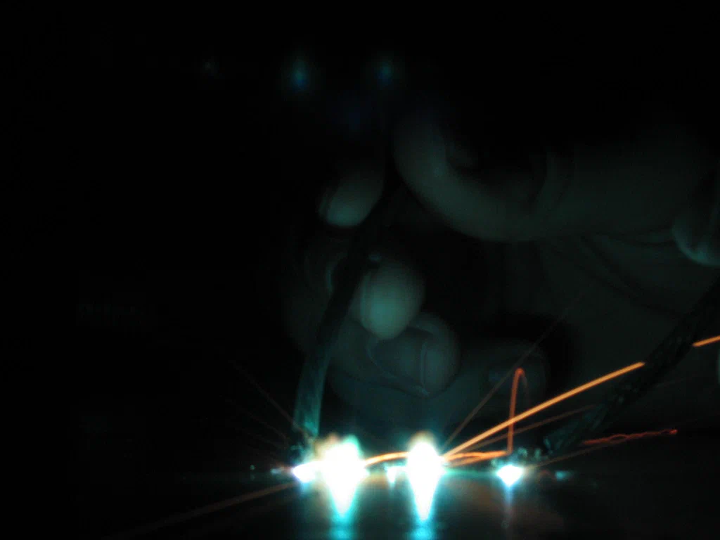 A person is welding or working with a high-voltage device, producing bright sparks and electric arcs in a dark environment.