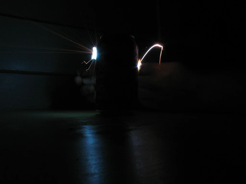 A high-voltage device sparking in an otherwise dark environment, with visible electrical arcs and sparks emanating from the device.