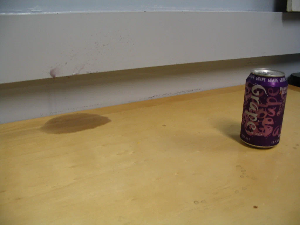 A soda can is placed on a wooden surface, with sparks and electrical discharge visible above, indicating a high-voltage electrical event.