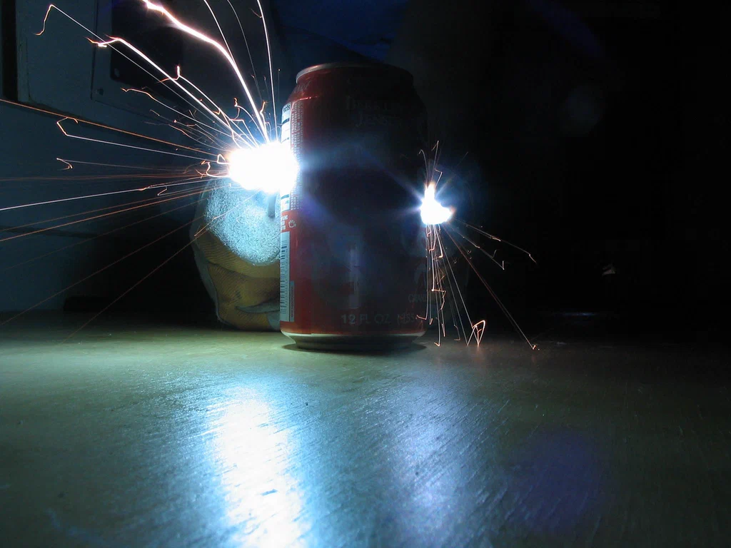 A can of soda is placed on a table with a device sparking and creating electrical discharges around it.