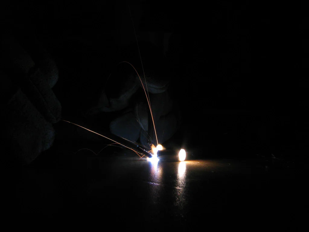 A high-voltage device sparking, with visible electrical sparks and bright points against a dark background.