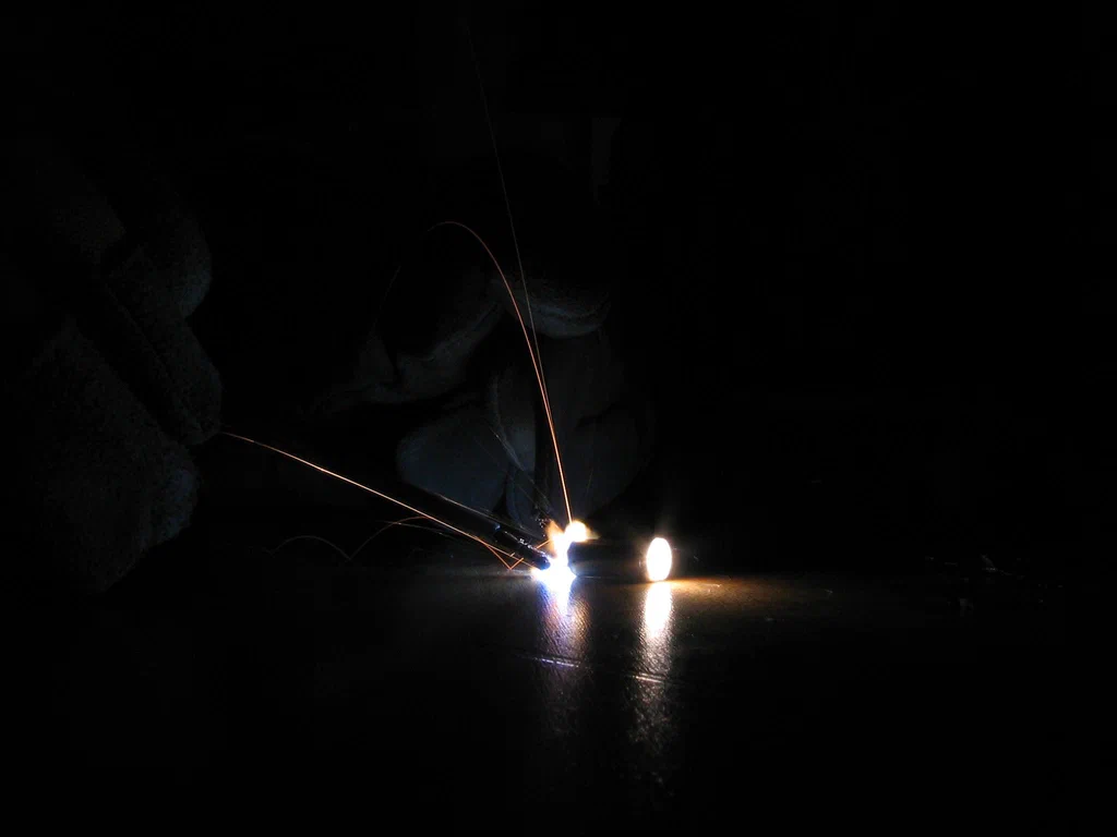A high-voltage device sparking, with visible electrical sparks and bright points against a dark background.