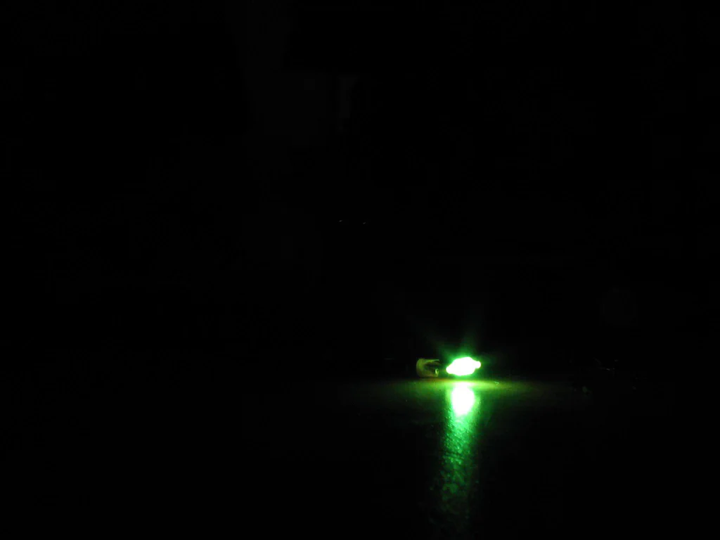 A high-voltage device is sparking, emitting a bright green arc of electrical discharge in a dark environment.