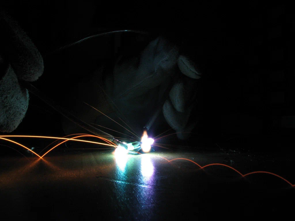 A close-up of a high-voltage device sparking, with bright arcs of electricity and sparks against a dark background.