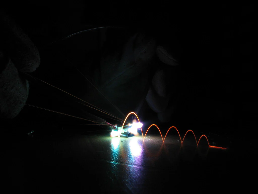 A high-voltage device sparking, with visible electrical arcs and sparks against a dark background.