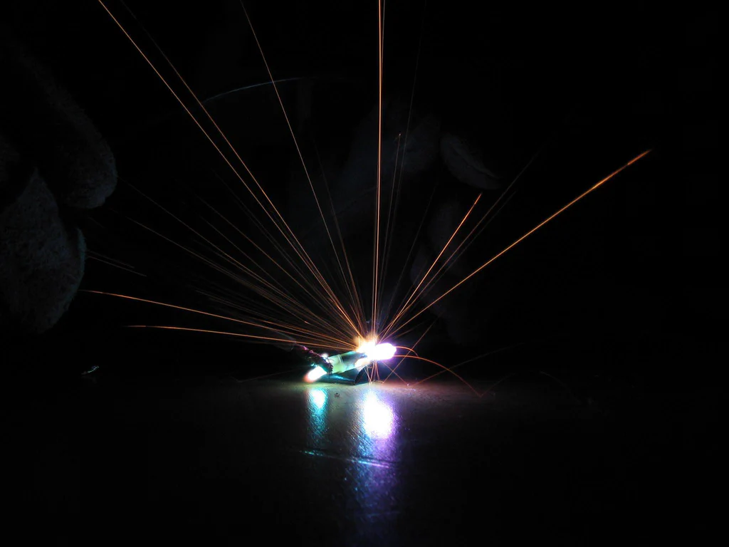A high-voltage device sparking with bright light and extending orange sparks into a dark background.