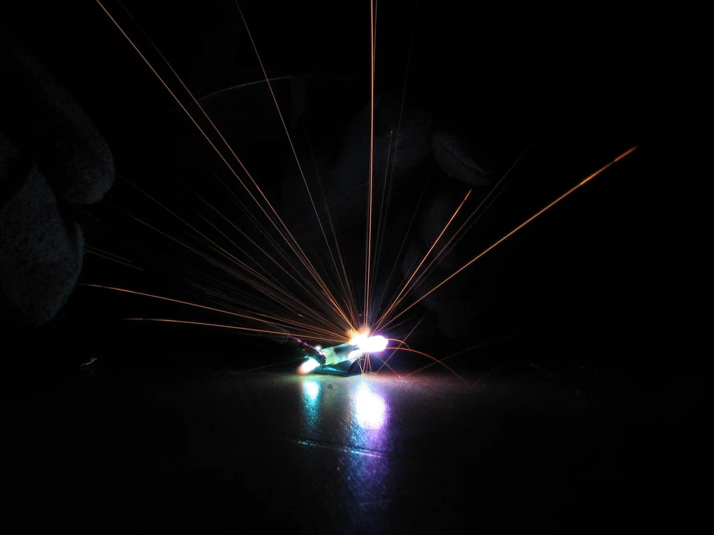 A high-voltage device sparking with bright light and extending orange sparks into a dark background.