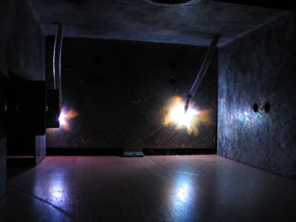 The image shows a high-voltage device sparking with bright electrical discharges in a dark enclosed space.