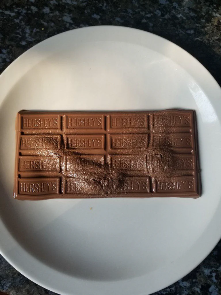 A white plate with a partially broken milk chocolate bar marked "HERSHEY'S" on a dark countertop.
