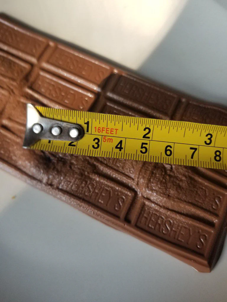 A close-up of a Hershey's chocolate bar with a measuring tape stretched across it, showing the size of the bar.