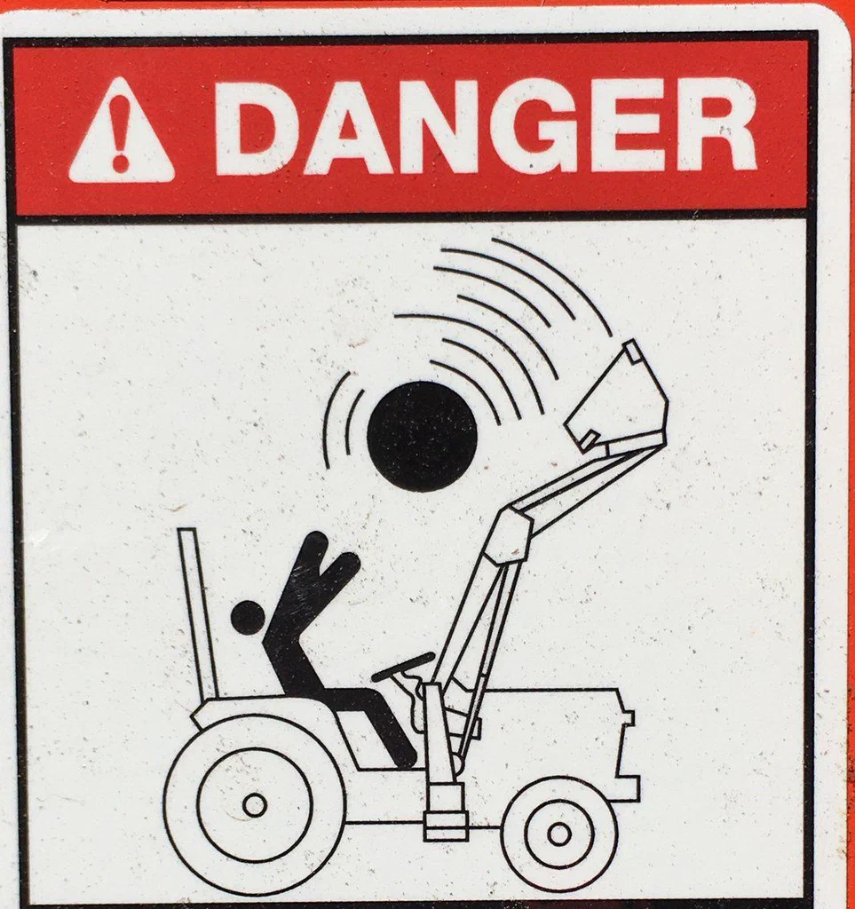 A warning sign with the word "DANGER" and a symbol of a person falling off a tractor due to a ball or object hitting the windshield.