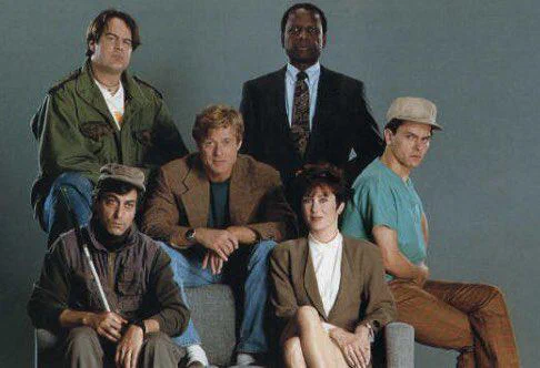 Six diverse individuals posing together in casual and professional attire against a plain background.