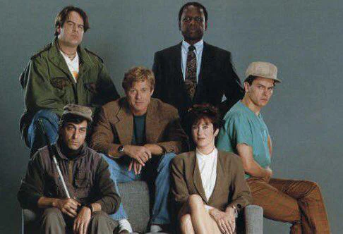 Six diverse individuals posing together in casual and professional attire against a plain background.