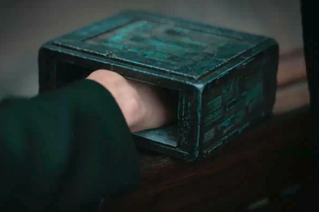 A hand reaching into a small, dark wooden box placed on a table.