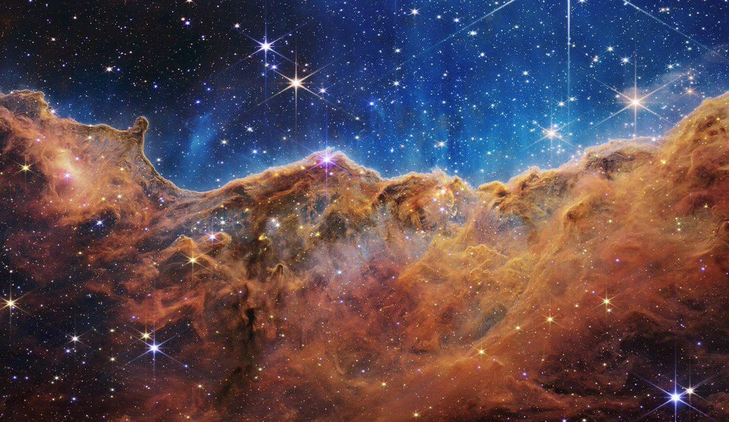 A view of a colorful, star-filled region of space with glowing nebulae and distant stars against a dark universe background.